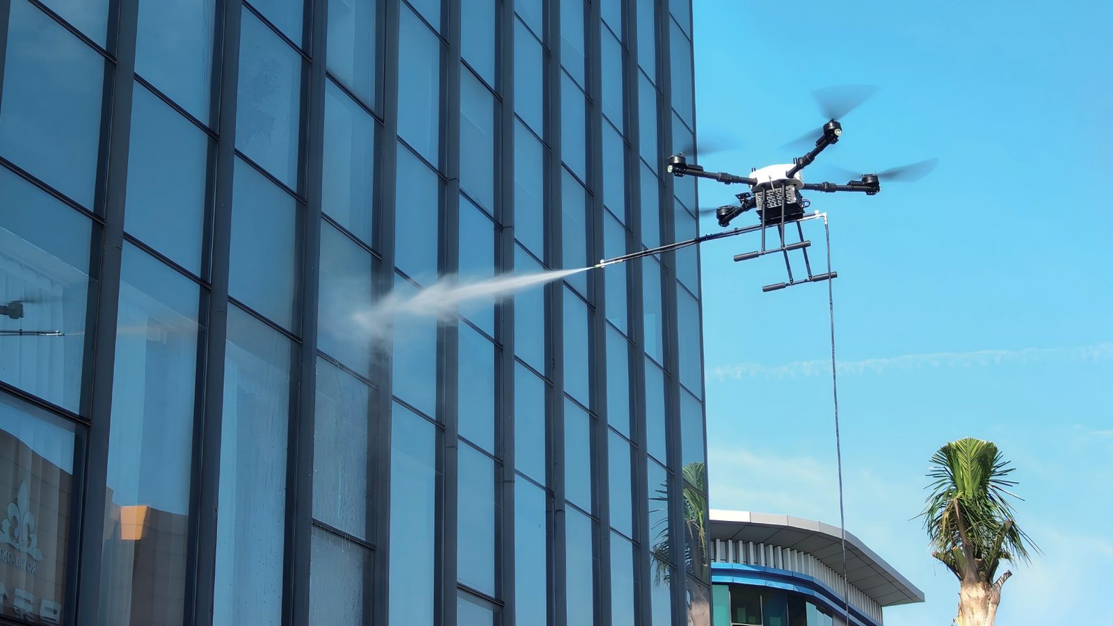 Tethered cleaning drone pressure washing the glass facade of a commercial office building